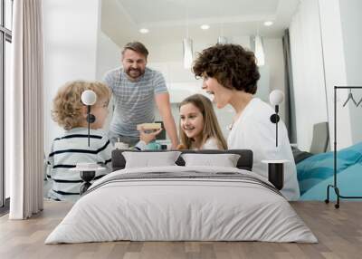 Portrait of happy young family with two children celebrating Valentines day  at home with adorable little boy giving presents in foreground Wall mural