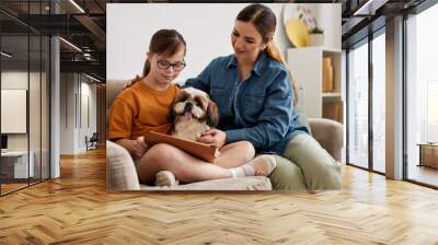 Portrait of loving mother and daughter with Down syndrome playing with dog while sitting on couch at home Wall mural