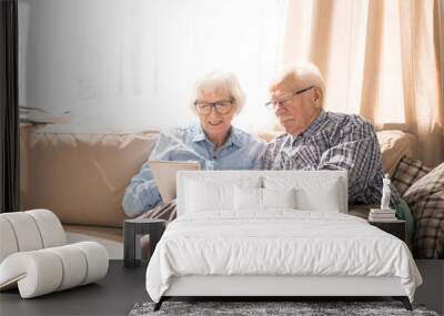 portrait of modern senior couple using digital tablet sitting on couch at home in sunlight copy spac Wall mural