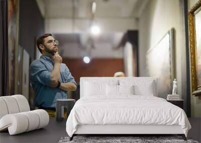 Portrait of pensive bearded man looking at paintings standing in art gallery or museum, copy space Wall mural