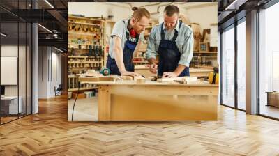 Portrait of senior carpenter teaching apprentice  standing at table in workshop, copy space Wall mural