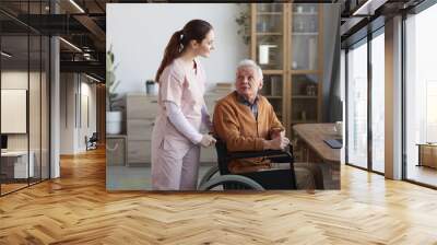 Portrait of senior man in wheelchair looking at caregiver helping him, copy space Wall mural