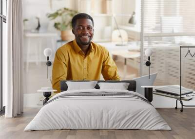 Portrait of smiling African-American man using laptop and looking at camera while enjoying work in minimal office interior, copy space Wall mural