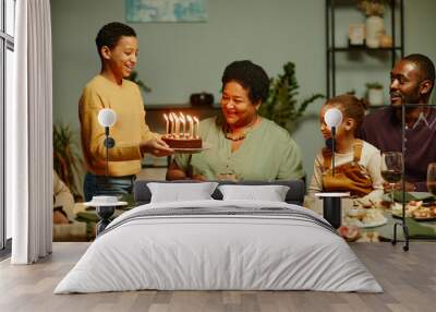 Portrait of smiling teenage boy bringing Birthday cake to happy African-American grandmother celebrating with family Wall mural