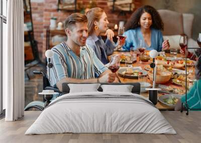 Portrait of smiling young man in wheelchair enjoying dinner party with friends and holding wineglass, copy space Wall mural