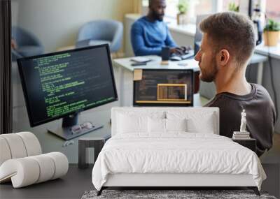 Portrait of software engineer writing code at workplace in office with multiple devices Wall mural