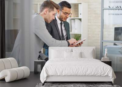 Portrait of successful Middle-Eastern entrepreneur using digital tablet while working with colleague leaning on desk in modern office of startup company Wall mural