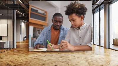 Portrait of teenage African-American boy doing homework or studying at home while sitting at desk with father helping him Wall mural