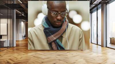 Portrait of trendy African man wearing headphones and using smartphone while posing in beautiful building outdoors, copy space Wall mural