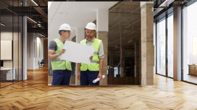 Portrait of two building contractors discussing plans while standing on construction site, copy space Wall mural