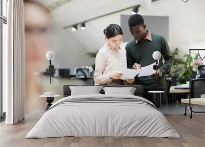 Portrait of two business interns discussing documents standing in modern office, copy space Wall mural