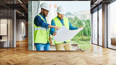 Portrait of two construction workers wearing hardhats discussing project holding engineering plans on site, copy space Wall mural