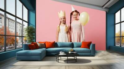 Portrait of two girls wearing party hats posing against pink background, copy space Wall mural