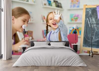 Portrait of two little girls enjoying art and craft lesson in development school and smiling happily to camera showing  hands in paint Wall mural