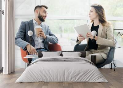 Portrait of two modern business people, man and woman, sitting in designer chairs and talking to each other in sunlit room Wall mural