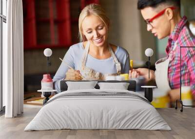 Portrait of two modern female artists enjoying  working together in art studio painting pictures, focus on pretty blonde woman smiling happily Wall mural