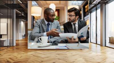 Portrait of two successful businessmen discussing deal while sitting at table in hotel lobby Wall mural