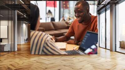 Portrait of two young people in business meeting at coffee shop focus on smiling Black man talking to colleague Wall mural