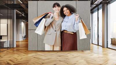 Portrait of two young women holding shopping bags and looking at camera smiling against minimal grey background Wall mural