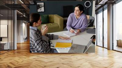 Portrait of two young women talking at table in office during casual work meeting and drinking coffee copy space Wall mural