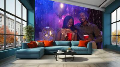 Portrait of young African-American couple smiling at camera while sitting on couch against sparkling background and enjoying party, copy space Wall mural