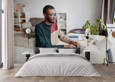 portrait of young african-american man wearing glasses while working from home and using laptop, cop Wall mural