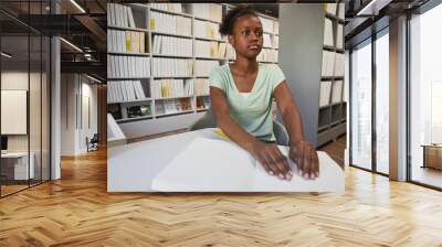 Portrait of young African-American woman reading Braille book in college library, copy space Wall mural