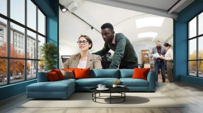 portrait of young african businessman using laptop with female colleague while working in office, co Wall mural