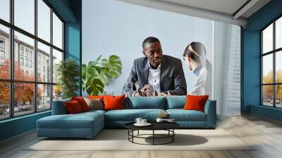 Portrait of young black businessman talking to female colleague during meeting in office against pale blue wall, copy space Wall mural