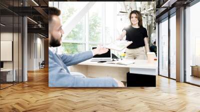 Portrait of young businesswoman handing graph to colleague sitting at meeting table in office Wall mural