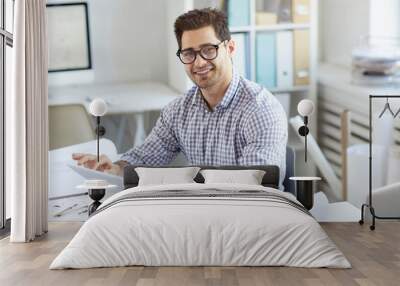 Portrait of young engineer smiling at camera while using digital tablet sitting at desk in office, copy space Wall mural