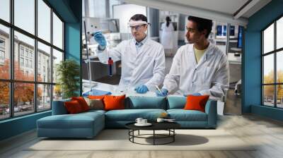 Portrait of young intern in scientific laboratory watching male scientist at work Wall mural