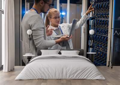 Portrait of young man and woman standing by server cabinets and discussing data while working with supercomputer in IT center Wall mural