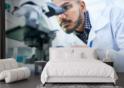 Portrait of young Middle-Eastern scientist looking in microscope while working on medical research in science laboratory, copy space Wall mural