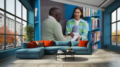 Portrait of young teenage girl talking to male therapist in college library and smiling Wall mural