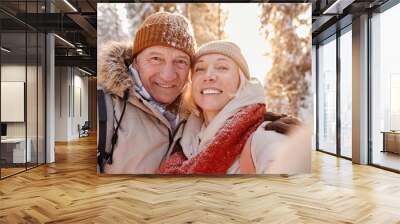 POV portrait of happy senior couple taking selfie photo while enjoying hike in winter forest Wall mural