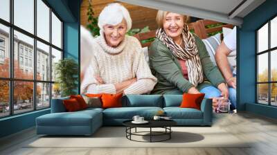 Pretty senior women with charming smiles listening to their male friend with interest while having gathering at cozy small patio Wall mural