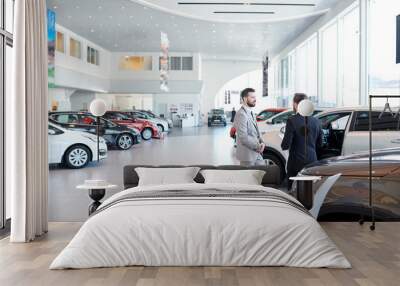 Professional salesperson selling new cars in a modern auto salon. Two men standing and choosing a new car Wall mural