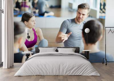 Serious pensive sporty guy with stubble sitting on floor and gesturing hand while sharing ideas for good training at yoga class Wall mural