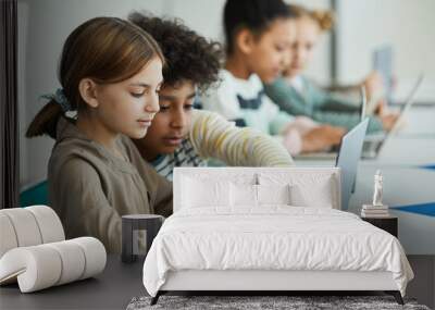 Side view at diverse group of children sitting in row at school classroom and using laptops Wall mural