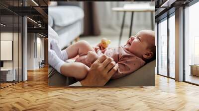 Side view of mother playing with laughing baby girl lying on her knees spending time at home Wall mural