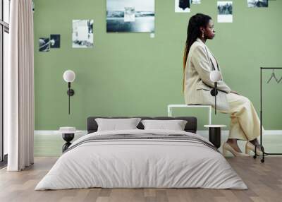 Side view of stylish young Black woman sitting on stool in modern art gallery looking at black and white photos on green wall Wall mural