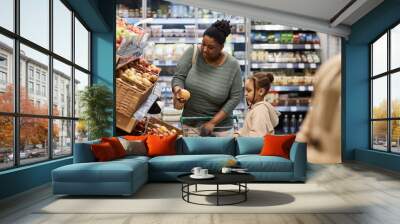 Side view portrait of black young woman with little girl shopping for groceries in supermarket and buying fruits Wall mural