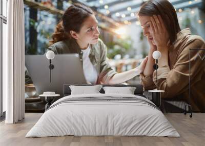 Side view portrait of frustrated young woman working at table in cafe with friend or colleague comforting her, copy space Wall mural