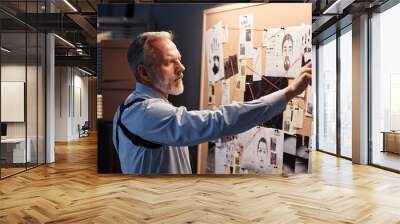 Side view portrait of handsome bearded detective standing by evidence board and studying leads in investigation Wall mural