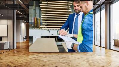 Side view portrait of handsome mature businessman signing investment paper in factory workshop standing with young workman wearing reflective jacket, copy space Wall mural