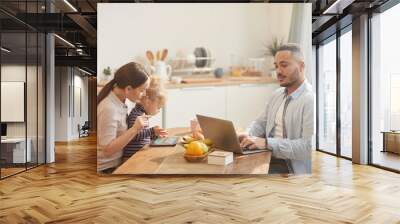 Side view portrait of modern father using laptop while enjoying family breakfast in cozy kitchen interior Wall mural