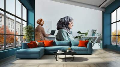 Side view portrait of modern Middle-Eastern woman wearing headscarf in office and using laptop, copy space Wall mural