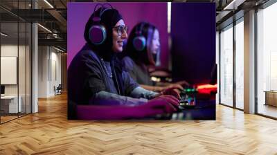 Side view portrait of Muslim young woman playing video games in cybersports club and smiling happily, copy space Wall mural