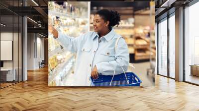 Side view portrait of smiling black woman buying groceries in supermarket and choosing dairy products Wall mural